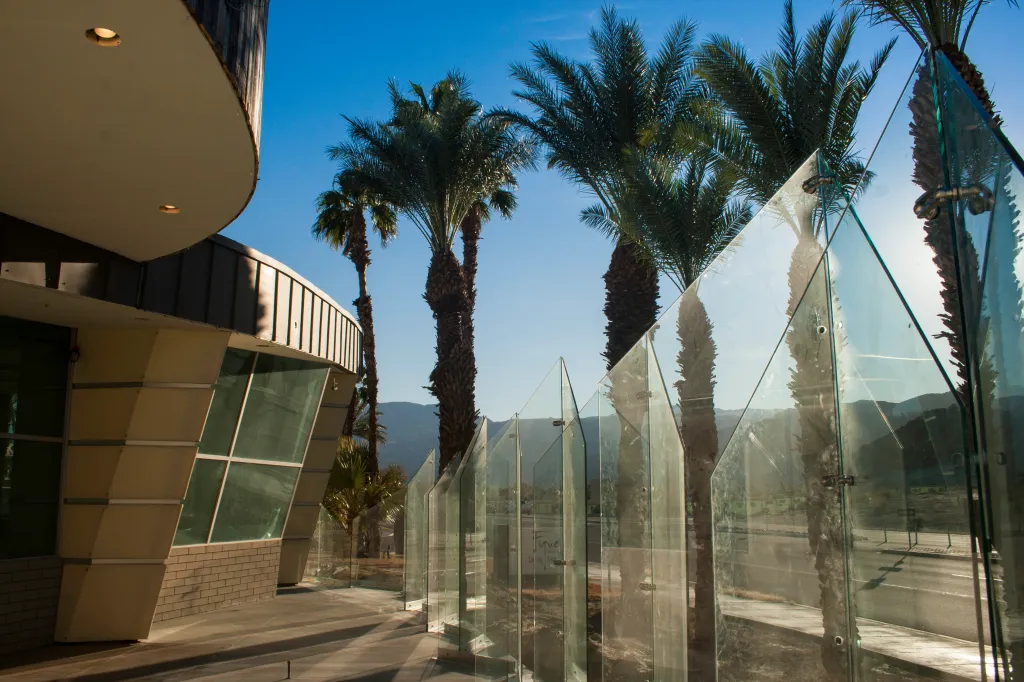 Modern building exterior with glass panel screens and tall palm trees against a clear bright blue sky